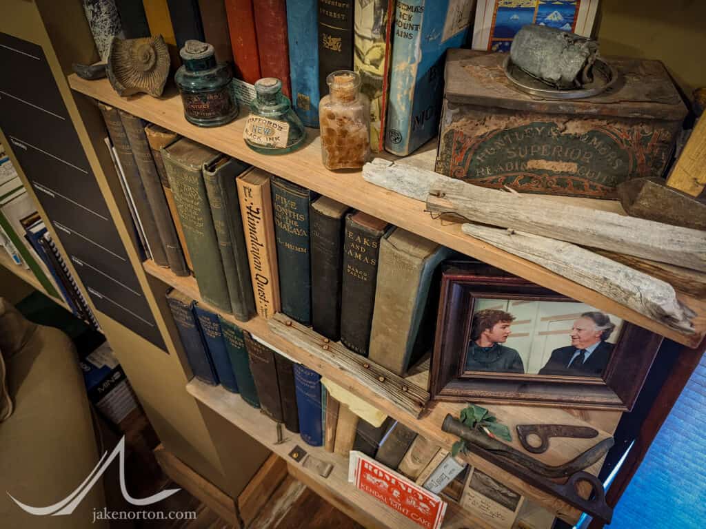 Bookshelf in my office containing the fascinating trash/treasure collected over the years, including a battery from 1922, Everest postcard from 1924, a pill bottle from 1933, piton from 1938, piton hammer from 1960, and more.