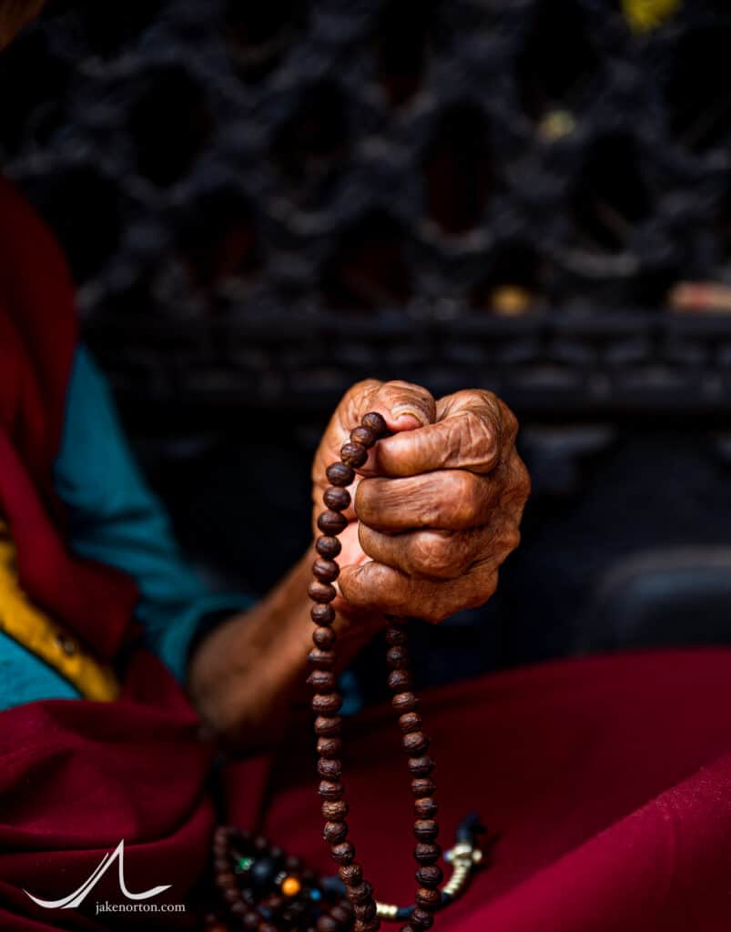 An elderly Tibetan Buddhist nun prays with her malla outside Bodhanath Stupa, Kathmandu, Nepal.