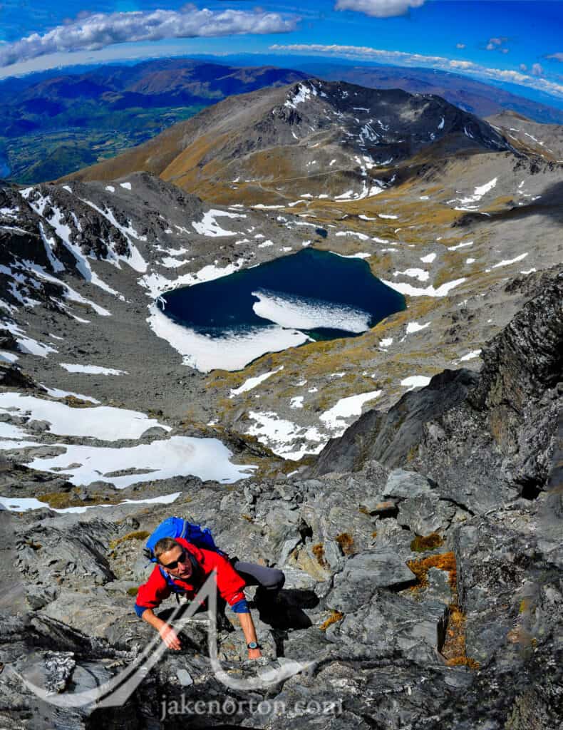 Charley Mace climbs on the Grand Traverse high in the Remarkables, Otago, New Zealand, with Lake Wakatipu behind.
