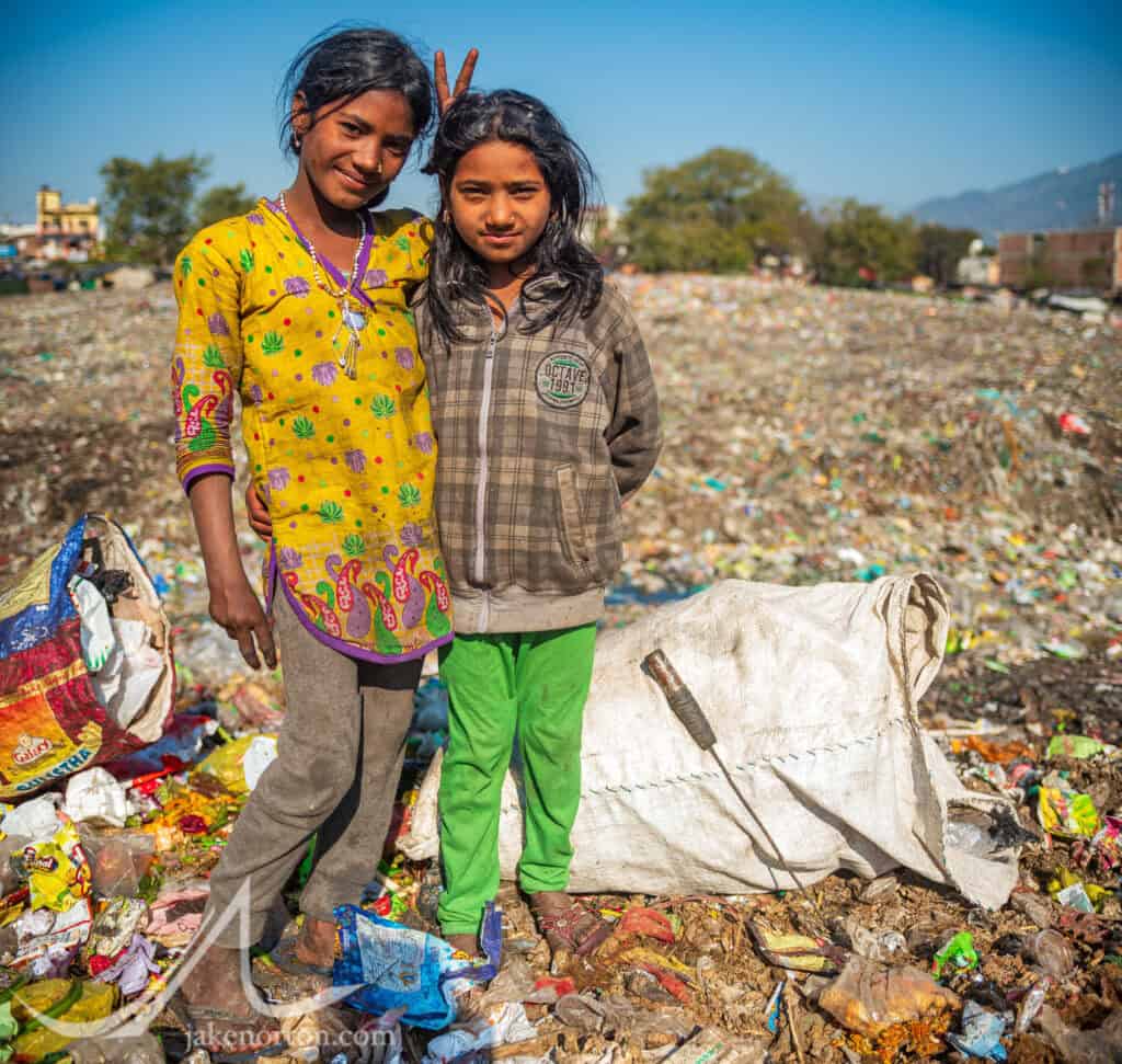 Jumila (left), a 10 year old Dalit girl, stands with her friend in the trash dump outside Rishikesh, India. Wonderful young girls, their lives revolve not around school and sports and play, but picking recyclables from mountains of trash to earn a few rupees for their families.